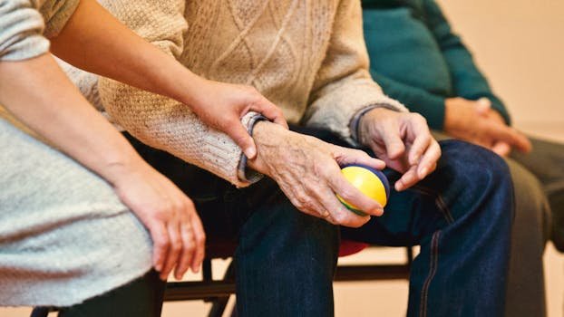 pexels-photo-339620-339620 An elderly person receives support from a caregiver, holding hands indoors, showcasing compassion.